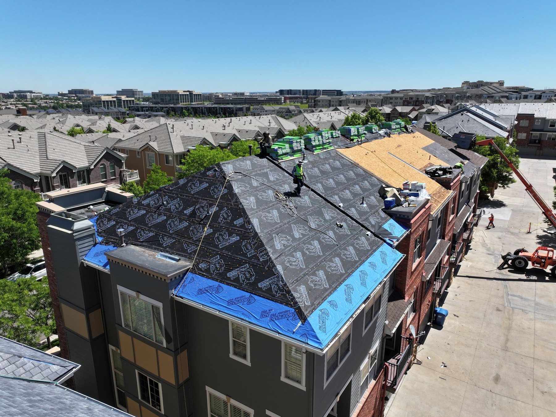 Fixins crew installing new underlayment on a multifamily re-roof overlooking a Colorado Springs neighborhood