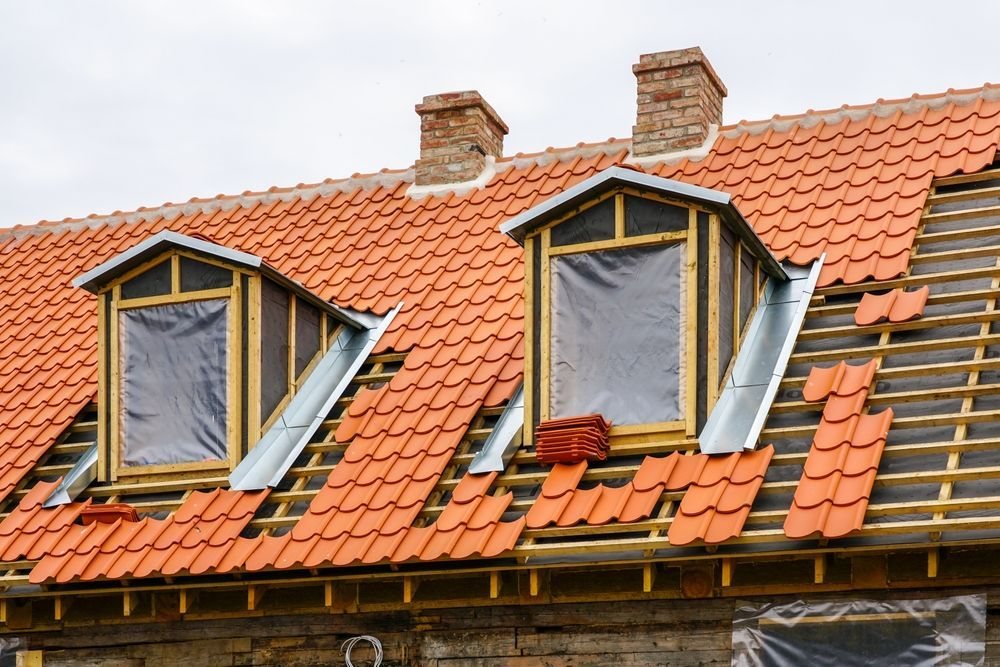 Clay tile roof being installed over battens with two dormers and brick chimneys