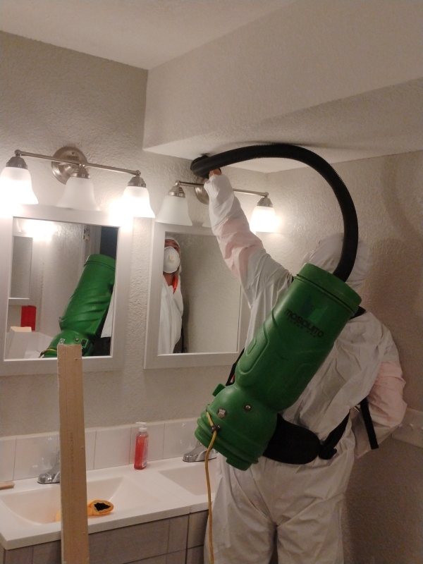 Fixins technician in a protective suit and respirator running a HEPA vacuum during bathroom mold remediation