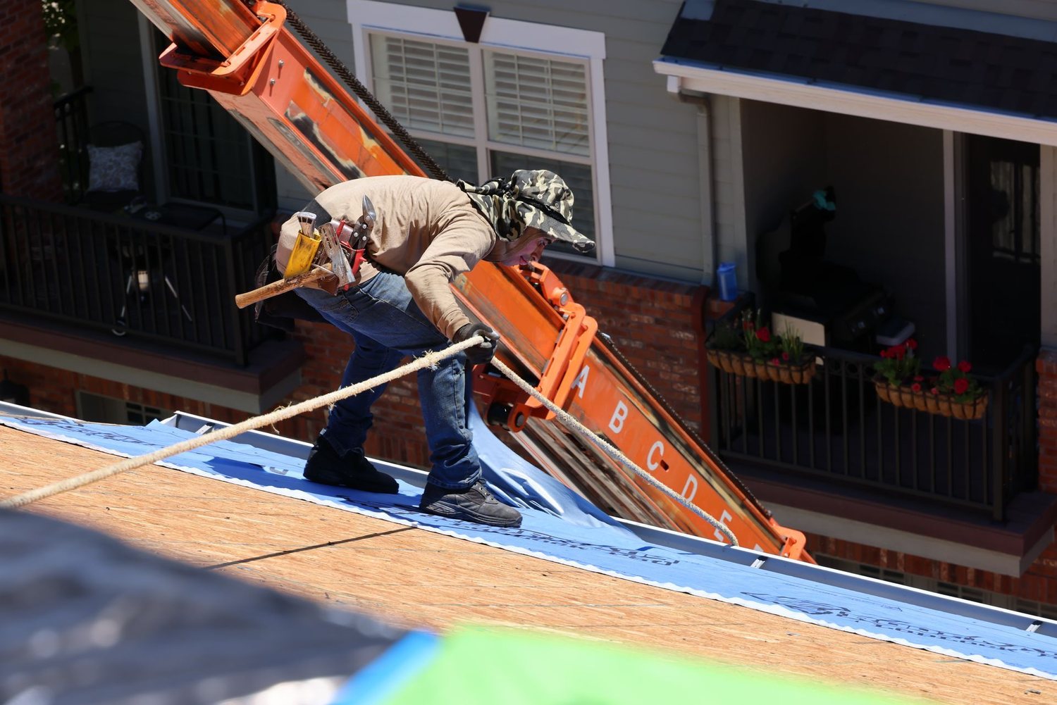 Roofer rolling synthetic underlayment across fresh roof decking during a reroof