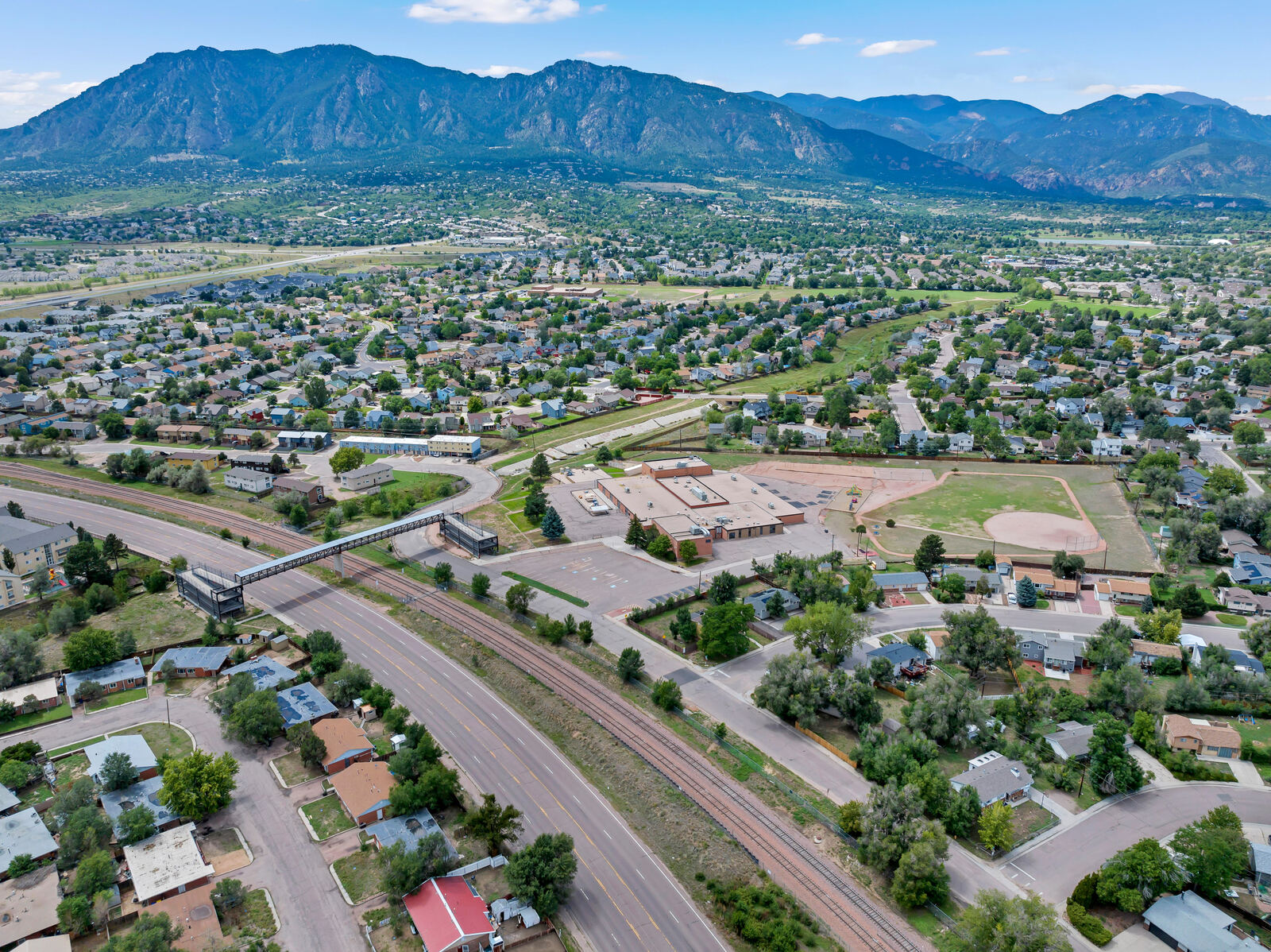 Aerial view of a Fort Carson area neighborhood with a school, rail line and the Front Range beyond
